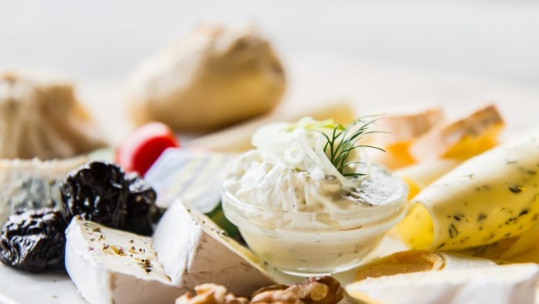 Nahaufnahme einer K&auml;seplatte mit verschiedenen K&auml;sesorten, N&uuml;ssen, Trockenfr&uuml;chten und einem Dip.