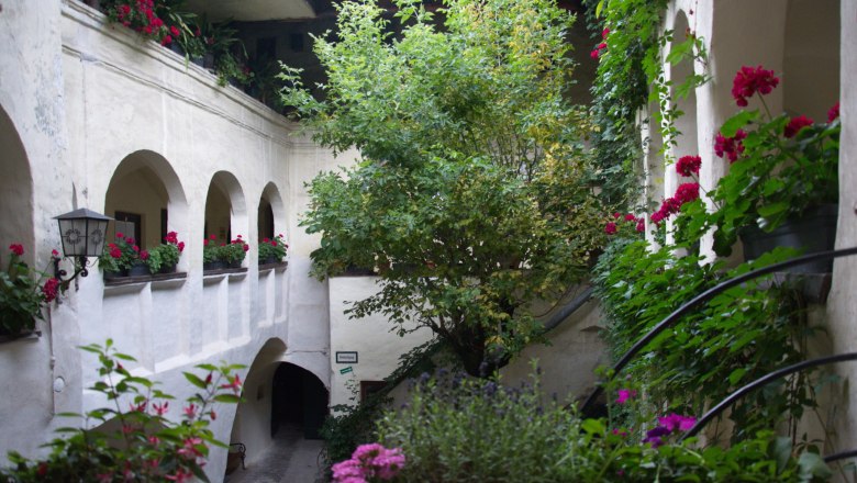 Innenhof, © Einzinger GmbH Ein Innenhof mit Pflanzen und Blumen in Töpfen, umgeben von weißen Wänden und Bögen.