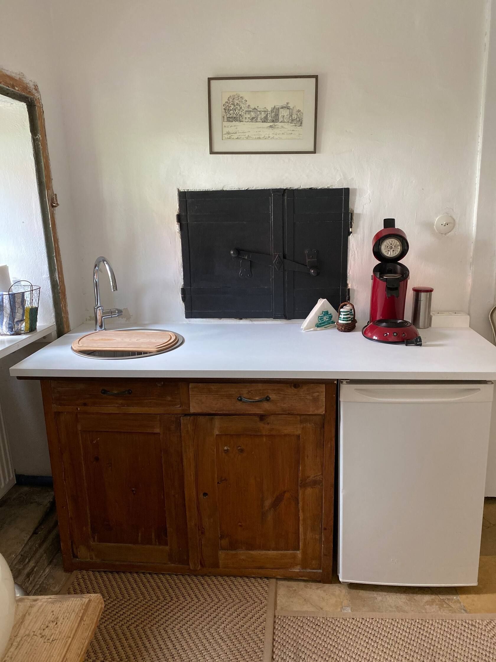Kleine Küche mit Holzschränken, weißer Arbeitsplatte, roter Kaffeemaschine und kleinem Kühlschrank.