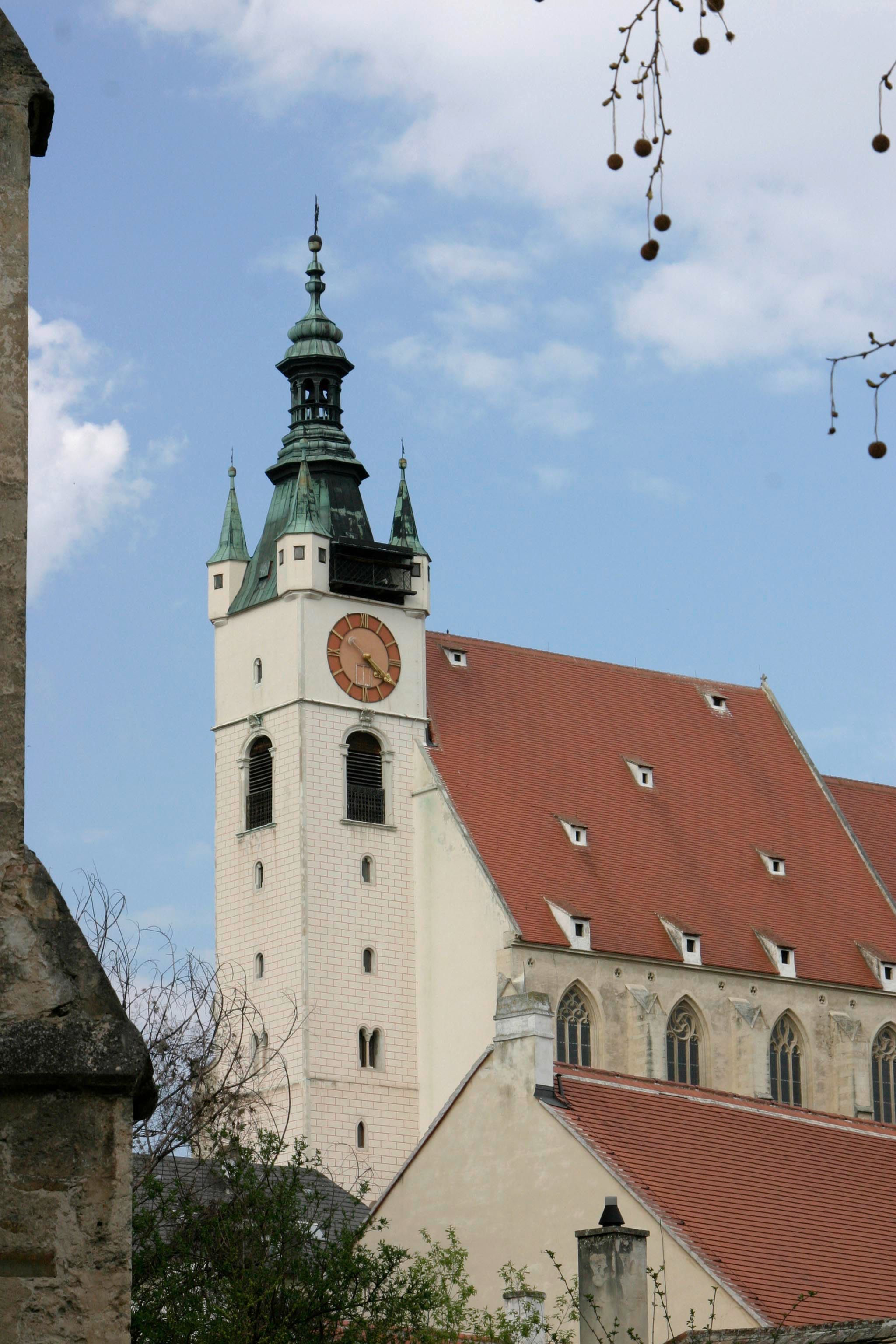 Piaristenkirche mit Turm und Uhr vor blauem Himmel.
