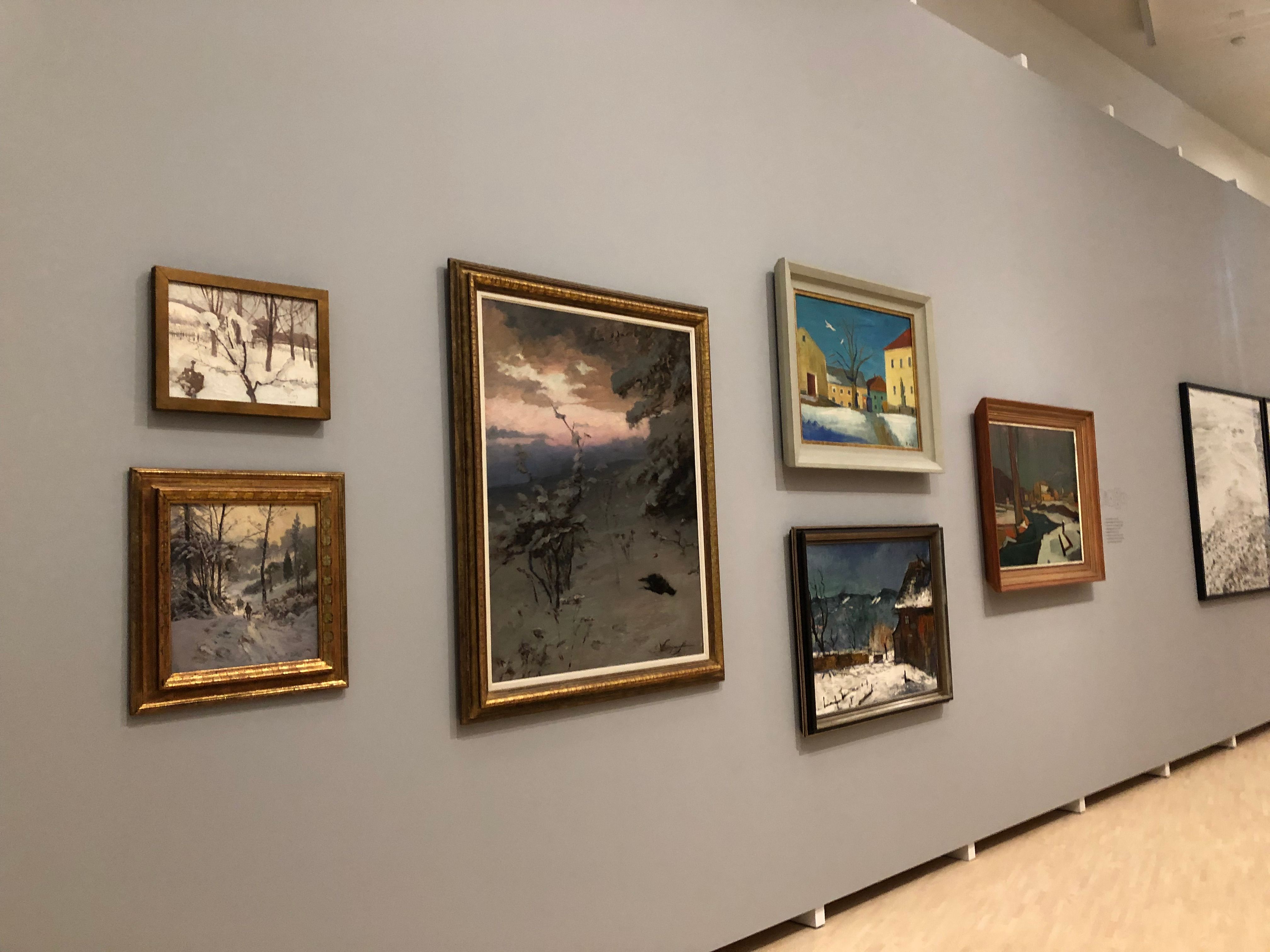 Eine Wand in einer Galerie mit mehreren Gemälden, die Winterlandschaften zeigen.