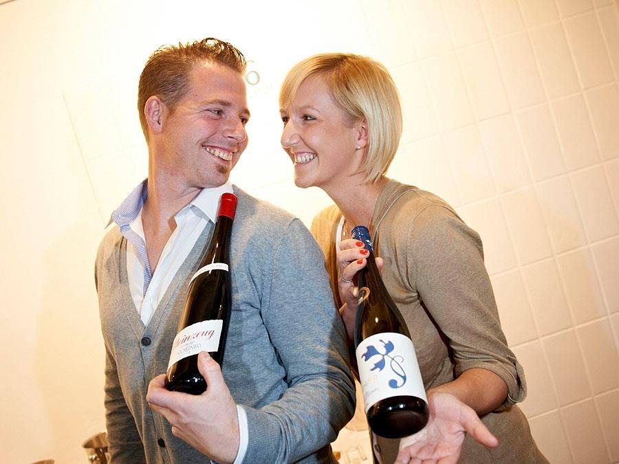 Ein Mann und eine Frau lächeln sich an und halten Weinflaschen in den Händen.
