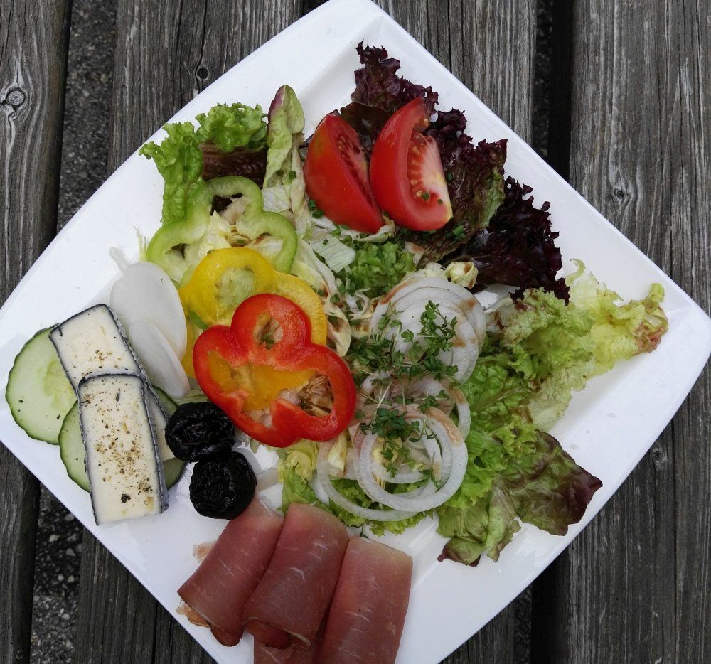 Ein Teller mit Salat, Tomaten, Paprika, Zwiebeln, Schinken und Käse auf einem Holztisch.