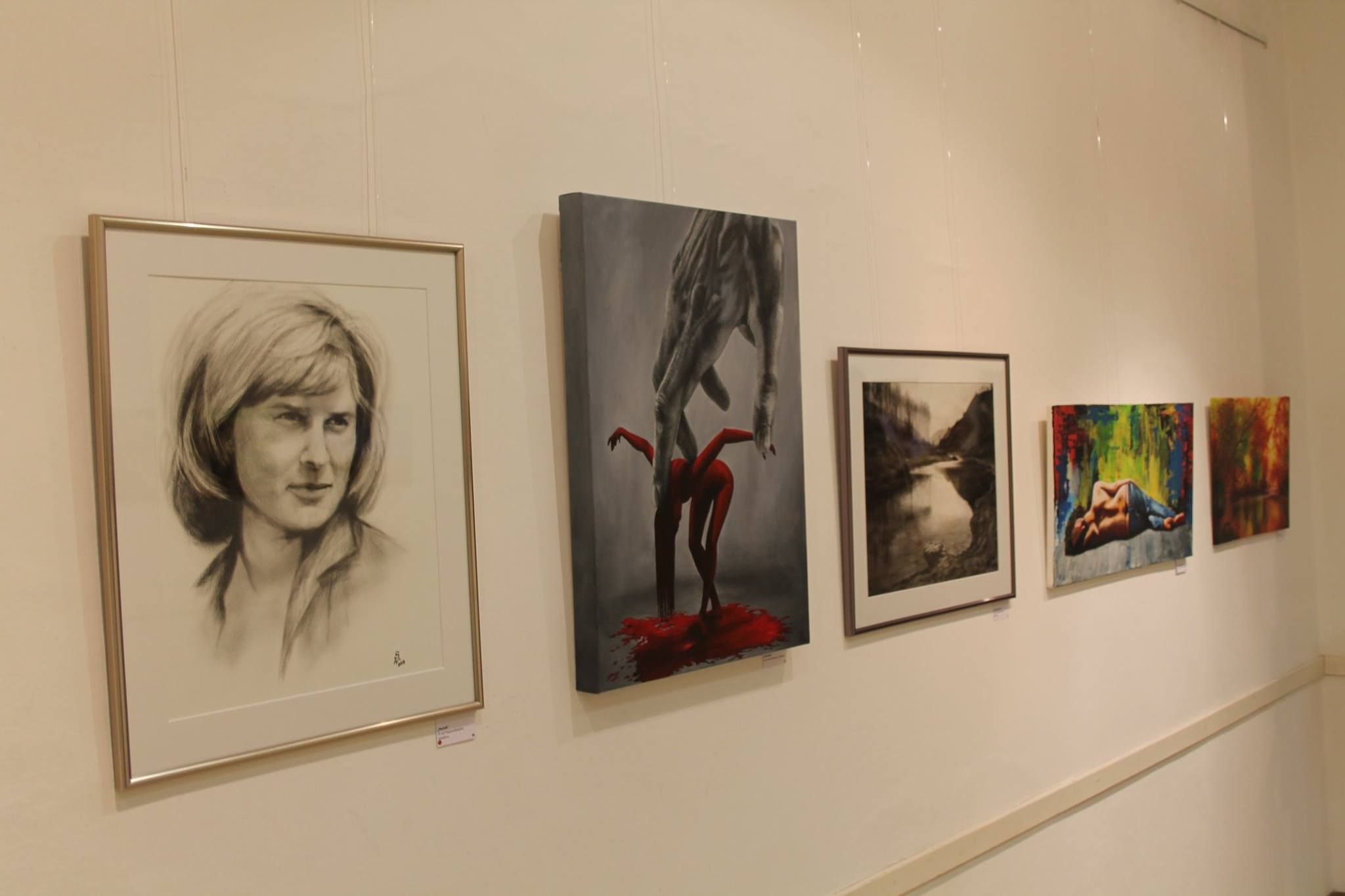Fünf Kunstwerke hängen an einer weißen Wand in einer Galerie.