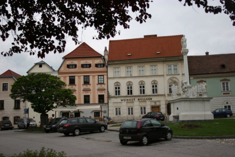 Historische Gebäude mit dem Schild 'Weingut Müllner' und einer Statue auf einem Platz.