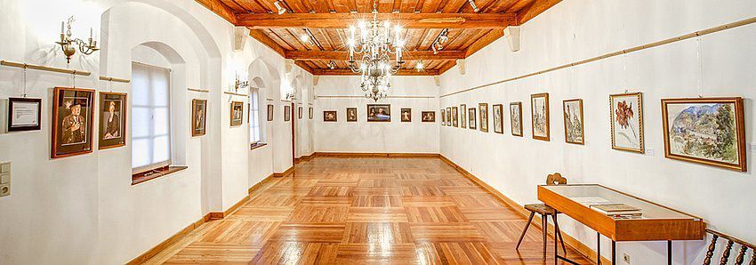 Ein eleganter Ausstellungsraum mit Holzboden, weißen Wänden und Gemälden an den Wänden.