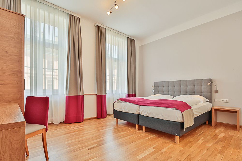 Helles Hotelzimmer mit Doppelbett, Schreibtisch und Stuhl.