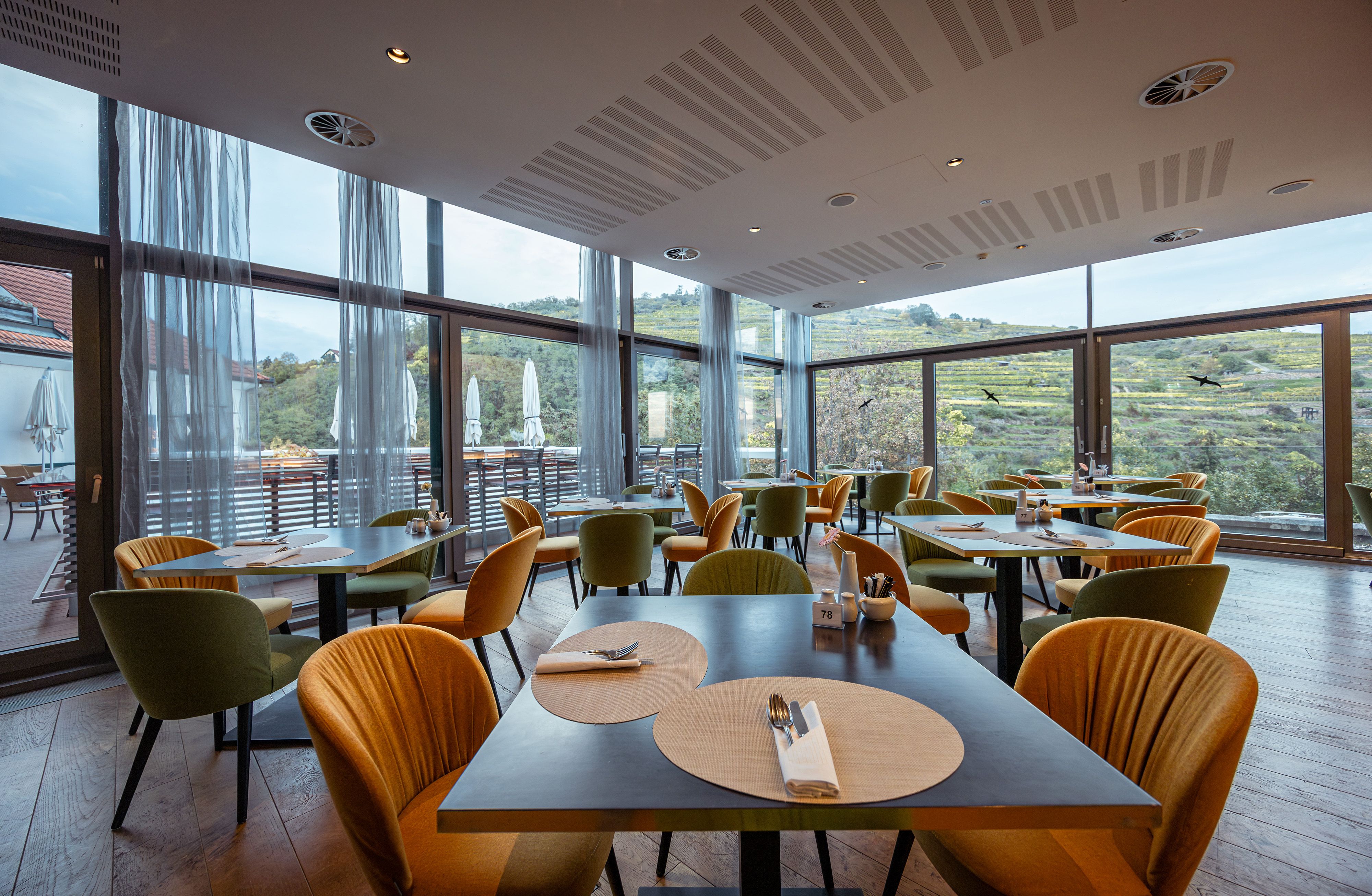 Innenansicht des modernen Restaurants mit großen Fenstern und Blick auf Weinberge.