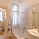 Helles Badezimmer mit Badewanne, Duschvorhang, Waschbecken und Fenster.