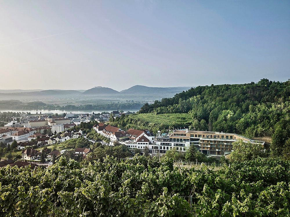 Blick auf das Steigenberger Hotel & Spa Krems umgeben von Weinbergen und Hügeln.