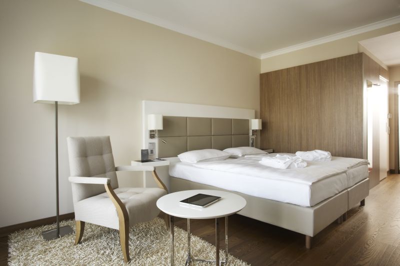 Modernes Hotelzimmer mit Doppelbett, Sessel, Tisch und Stehlampe.