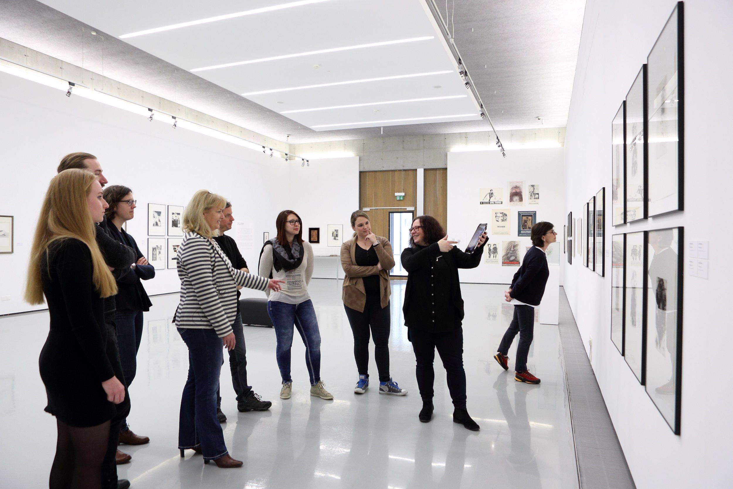 Gruppe von Menschen in einer Kunstgalerie, die Kunstwerke an der Wand betrachten.