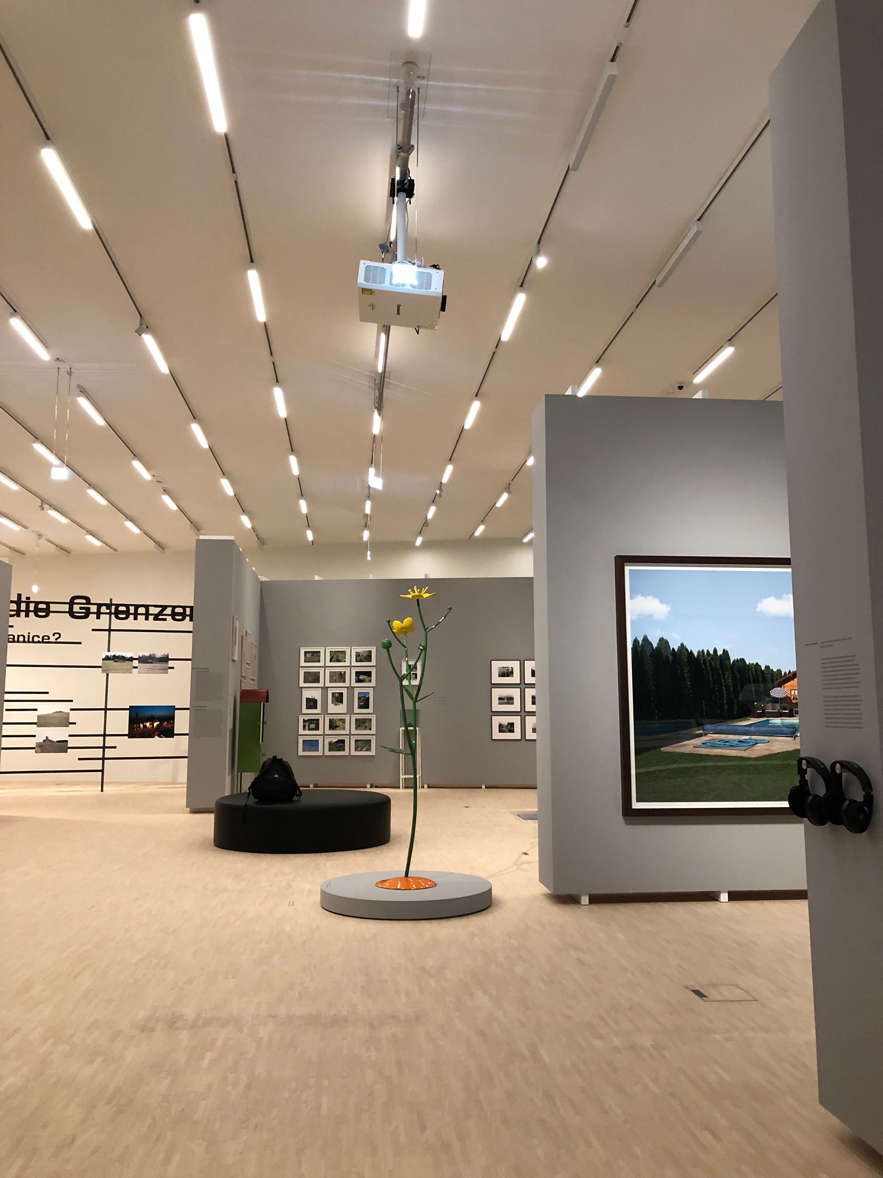 Innenansicht einer modernen Galerie mit Kunstwerken an den Wänden und einer Skulptur in der Mitte.