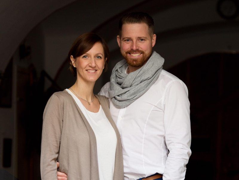 Ein lächelndes Paar steht nebeneinander, der Mann trägt einen Schal.