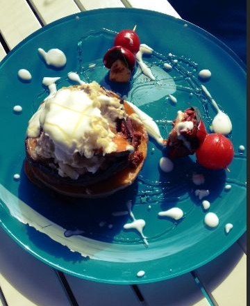 Ein blaues Teller mit einem Dessert, das aus Pancakes, Sahne und Kirschen besteht, auf einem Tisch.