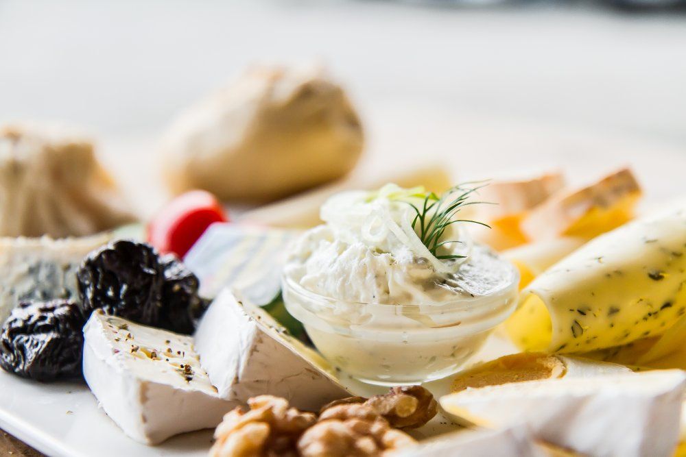 Nahaufnahme einer Käseplatte mit verschiedenen Käsesorten, Nüssen, Trockenfrüchten und einem Dip.