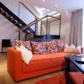 Modern suite with orange couch, decorative cushions and staircase in the background.