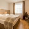 Hotel room with double bed, desk and window with curtains.