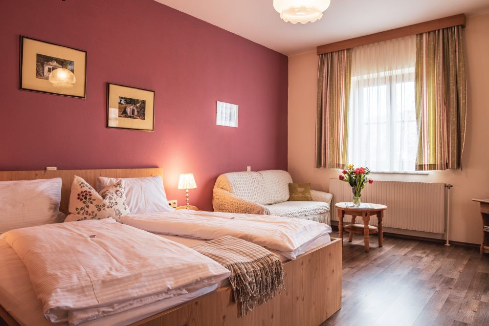 Gemütliches Gästezimmer mit Doppelbett, Sofa, Tisch und Blumenstrauß.