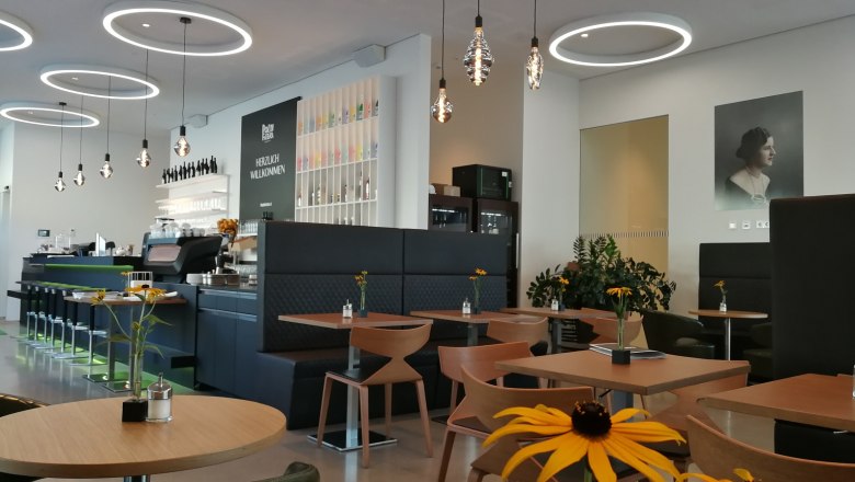 Innenansicht eines modernen Caf&eacute;s mit runden Deckenleuchten, Holztischen und Blumen auf den Tischen.