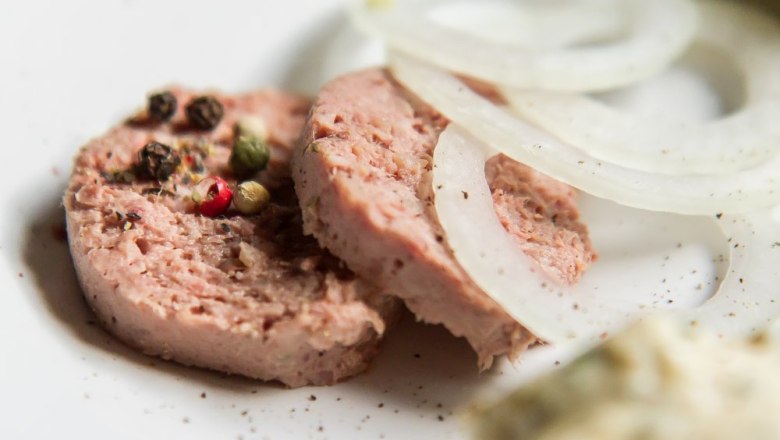 Nahaufnahme von Wurstscheiben mit Pfefferk&ouml;rnern und Zwiebelringen auf einem Teller.