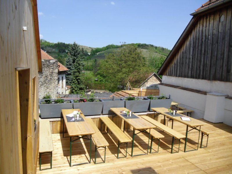 Holzterrasse mit Bänken und Tischen, umgeben von ländlicher Landschaft.