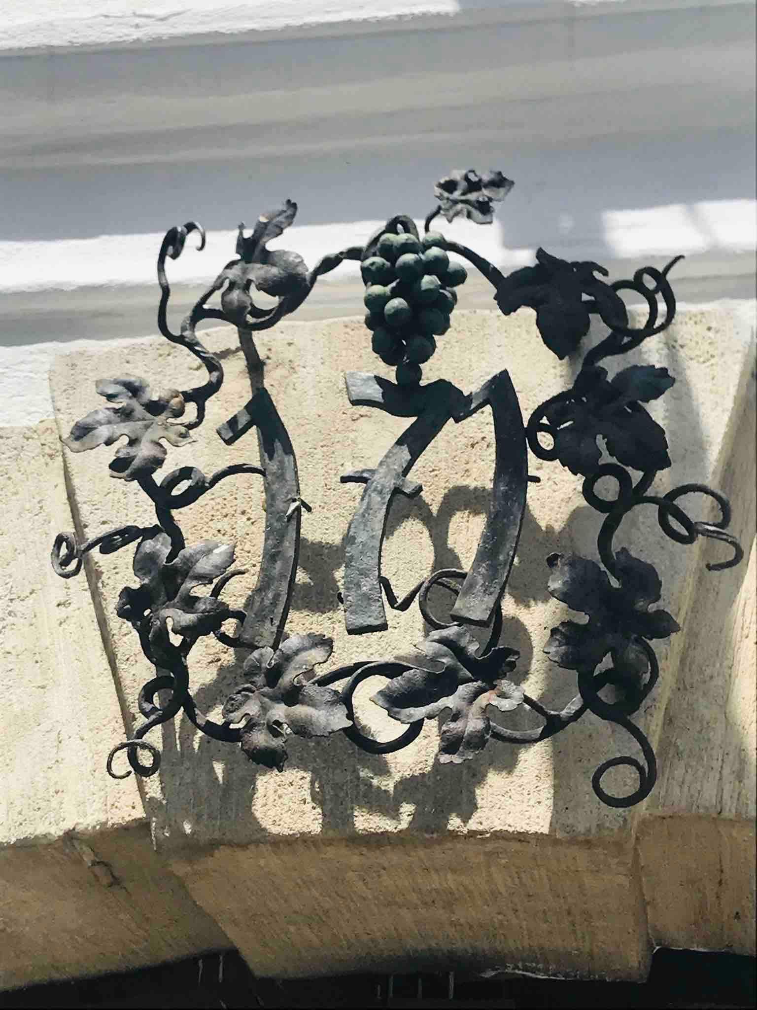 Metallverzierung mit Traubenmotiv und der Zahl 1717 auf einem Steinbogen.