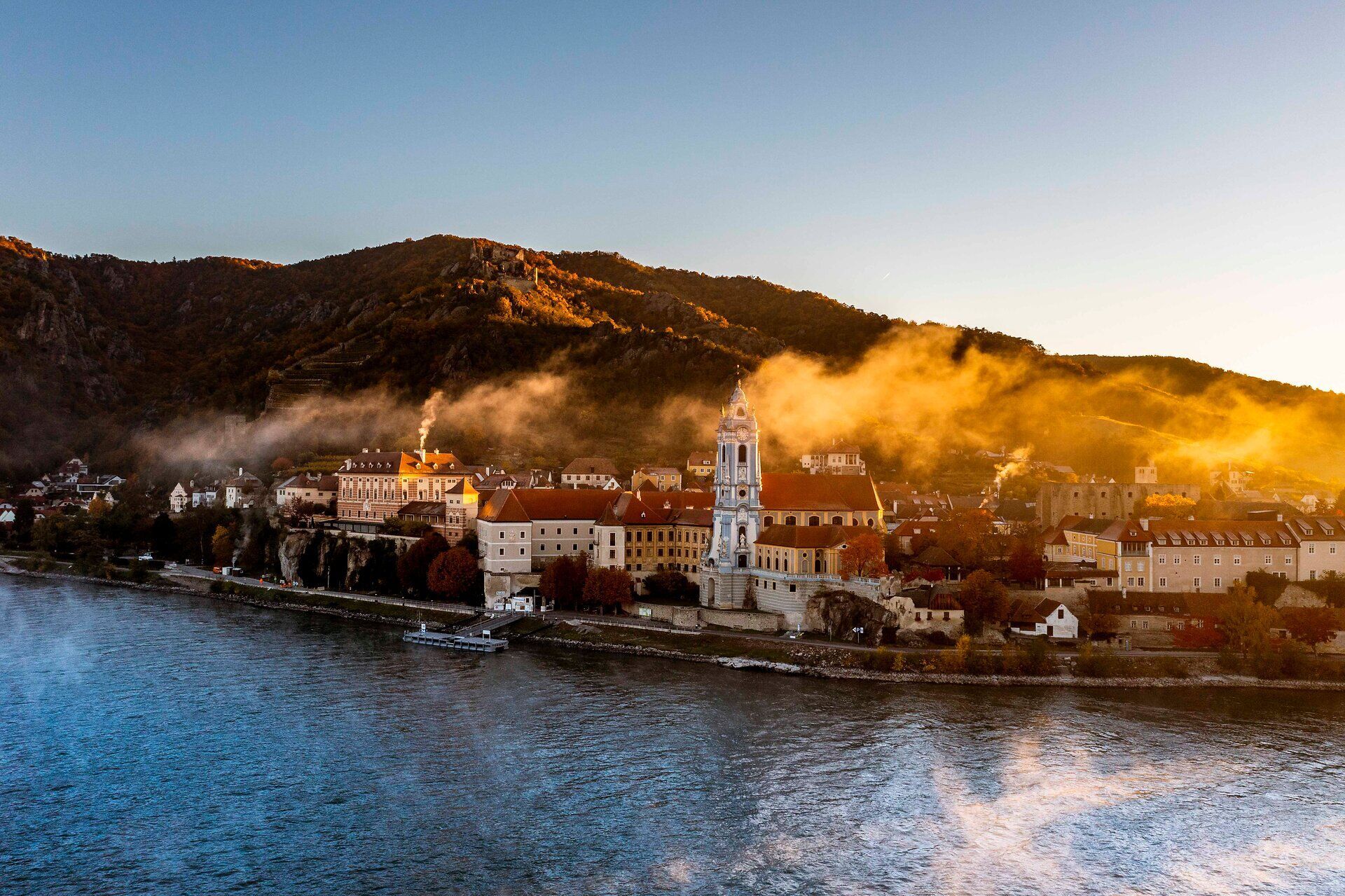 Die sanften Hügel umarmen das malerische Städtchen, während die Morgensonne die Nebelschwaden über der Donau vertreibt. Historische Gebäude und die beeindruckende Ruine verleihen der Szenerie einen Hauch von Romantik und laden zu einem unvergesslichen Spaziergang ein.