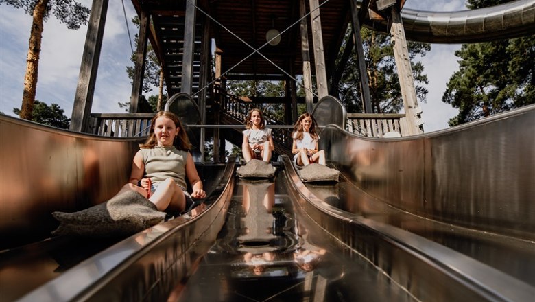 Three children slide down a metal slide in a park.