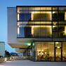 Modern hotel building with glass façade at dusk, illuminated interiors visible.