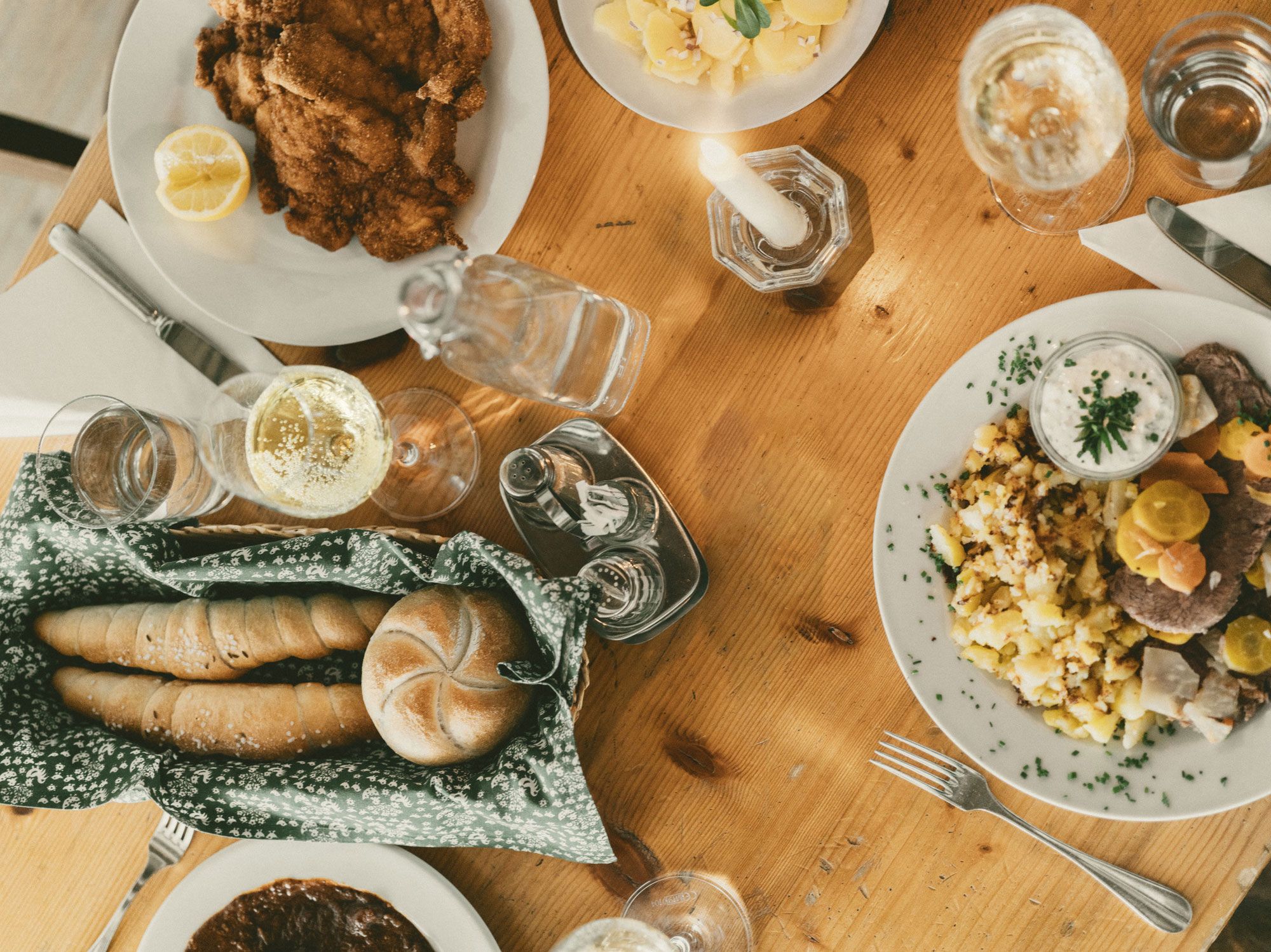 Gedeckter Tisch mit Schnitzel, Erdäpfelsalat und Getränken.