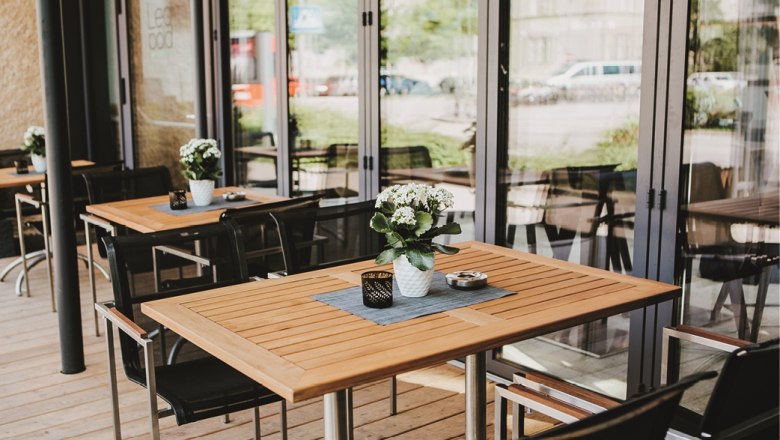 Terrace of a wine bar with wooden tables, chairs and flowers in pots.