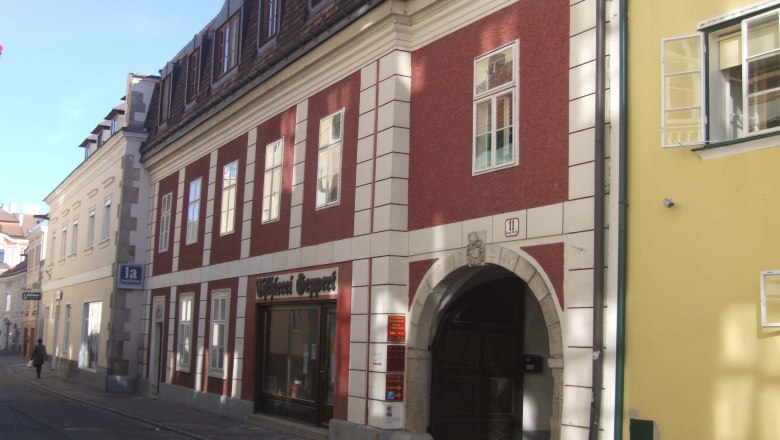 Historisches Geb&auml;ude mit roter Fassade und Torbogen in einer Stra&szlig;e.