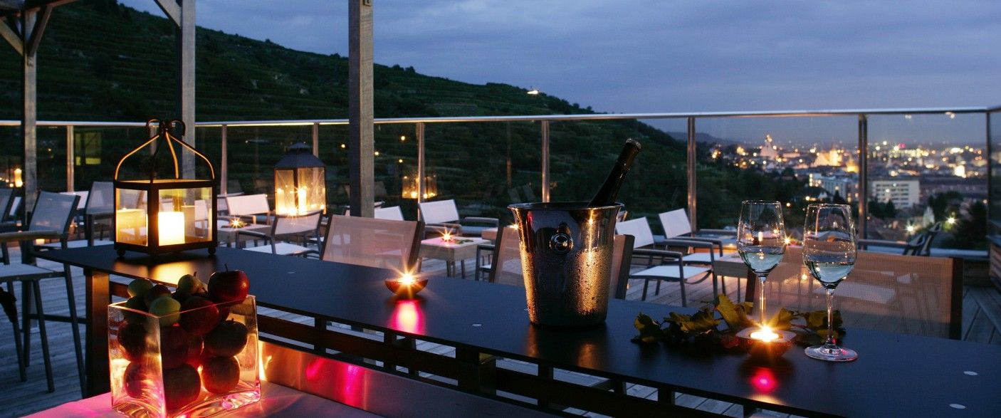 Abendliche Terrasse mit Kerzenlicht, Weingläsern und Blick auf eine Stadt.