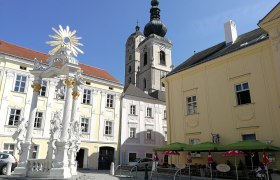 Historischer Platz mit barocker Säule, Kirche und Café.
