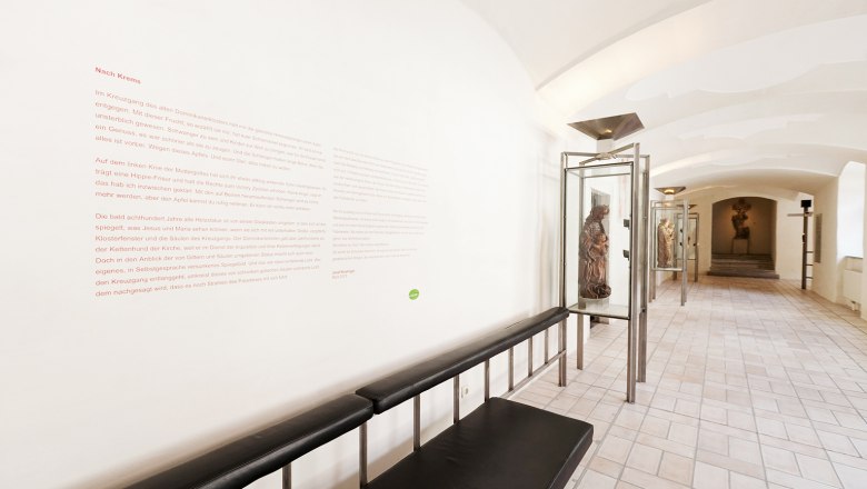 A museum corridor with sculptures in glass cabinets and a text on the wall.