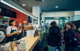 Eine Caf&eacute;-Mitarbeiterin bedient zwei Kundinnen an der Theke.