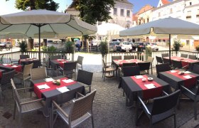 Au&szlig;enterrasse eines Caf&eacute;s mit Tischen und Sonnenschirmen auf einem gepflasterten Platz.