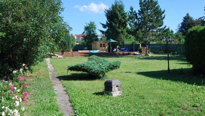 Garten mit Rasen, B&auml;umen und einem kleinen Weg, der zu einem Holzhaus f&uuml;hrt.