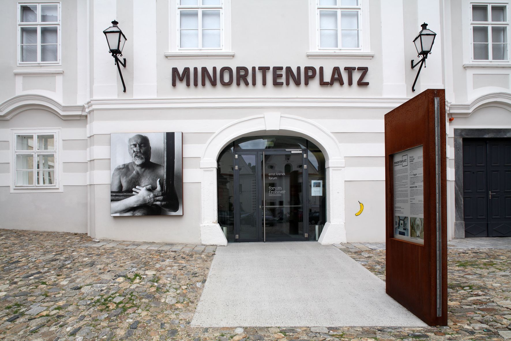 Eingang zum Forum Frohner am Minoritenplatz mit Kunstwerk und Infotafel.