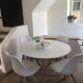 Modern seating area with round table and four white chairs in a bright room.