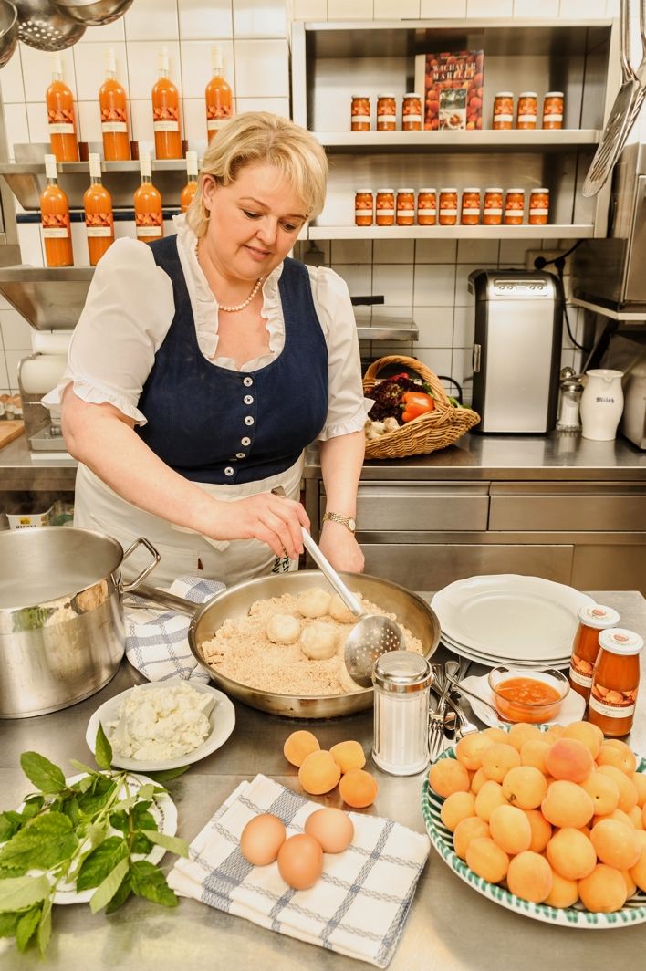 Frau in traditioneller Kleidung kocht in einer Küche mit regionalen Zutaten.