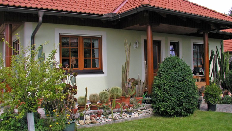 A house with a red tiled roof, surrounded by a garden with cacti and shrubs.