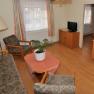 Wohnzimmer mit Sofa, zwei Sesseln, Tisch mit Pflanze, Fernseher und Zugang zu einem Schlafzimmer.