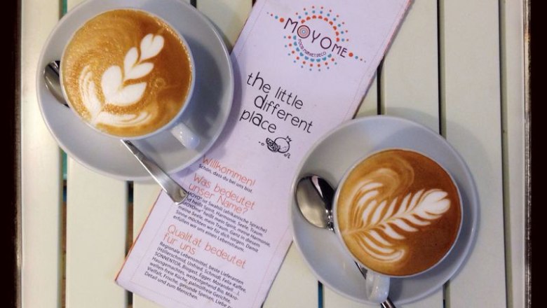 Zwei Cappuccinos mit Latte Art und ein Flyer auf einem Tisch.