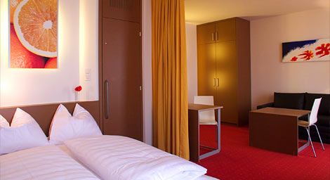 Hotelzimmer mit Doppelbett, rotem Teppich und moderner Einrichtung.