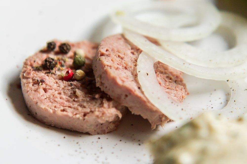 Nahaufnahme von Wurstscheiben mit Pfefferkörnern und Zwiebelringen auf einem Teller.