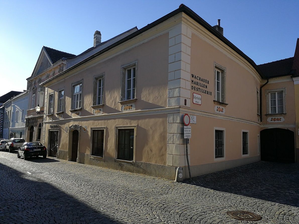 Historisches Gebäude mit der Aufschrift 'Wachauer Marillen Destillerie' in einer gepflasterten Straße.