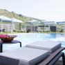 An outdoor pool with sun loungers and parasols in front of a hilly landscape.