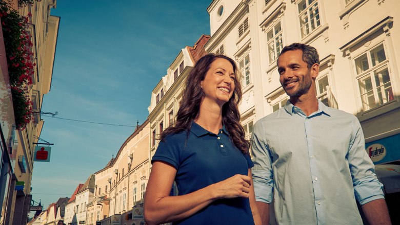 A smiling couple strolls through the old town of Krems in sunny weather.
